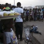 Bystanders stand around the body of a suspected Ebola victim lying in the street in the town of Koidu