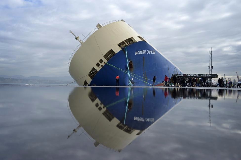 The cargo ship Modern Express is reflected in water on the dock as it lists at a mooring in the port of Bilbao, in Zierbena, northern Spain, February 4, 2016. The 164-meter vessel, which was transporting 3,600 tonnes of wood along with construction machinery, was towed to the port after spending six days listing and adrift in the Bay of Biscay. REUTERS/Vincent West